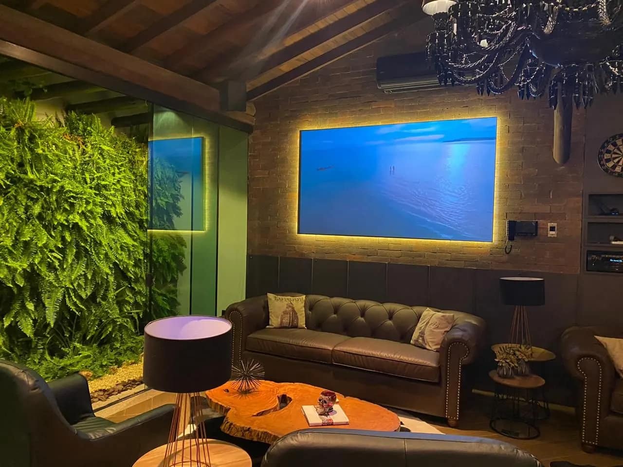 Sala de cinema residencial com tela iluminada por trás, sofá de couro e jardim vertical.